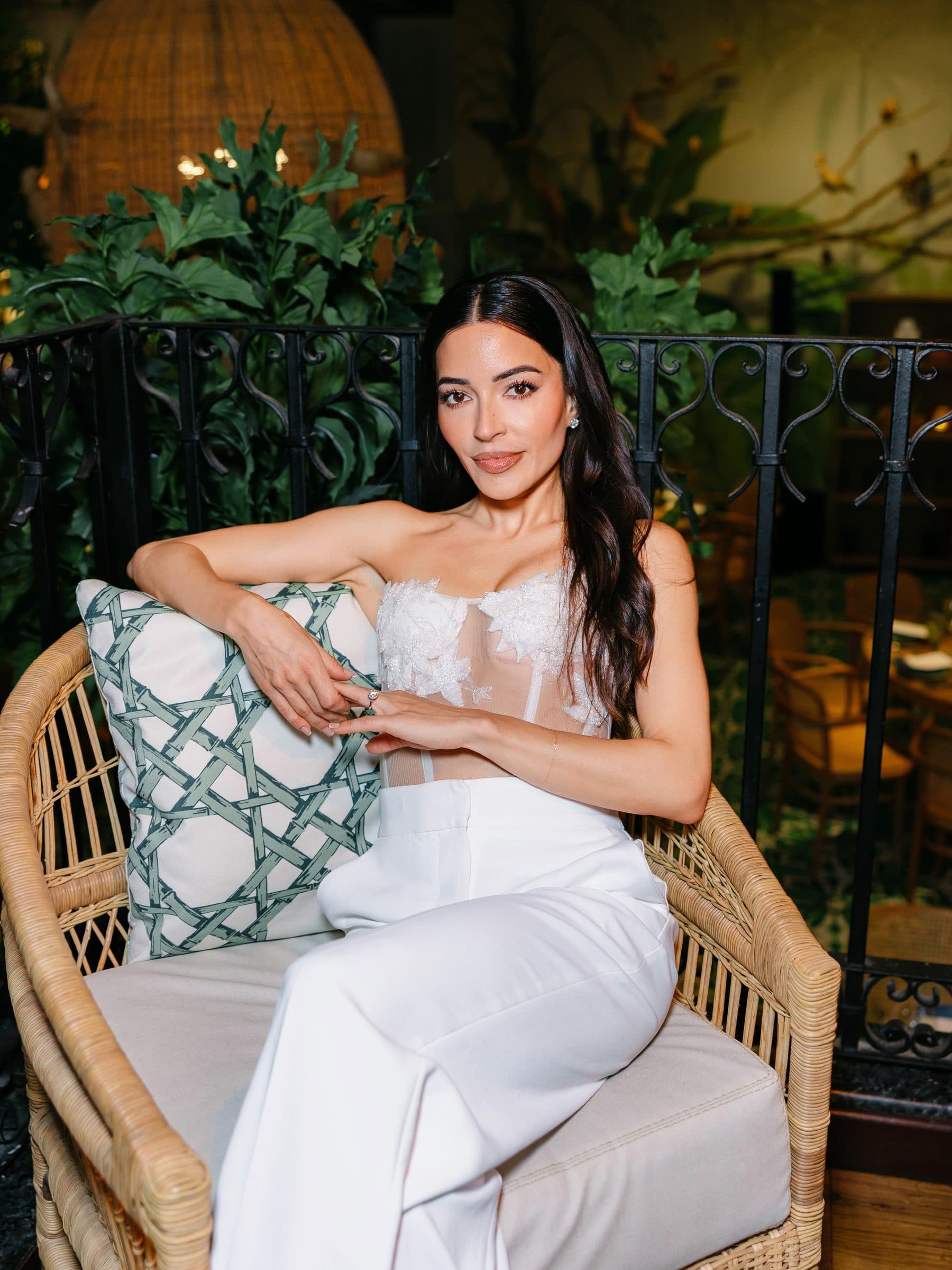 A bride seated in a wicker chair on a candlelit terrace, by Danilo & Sharon